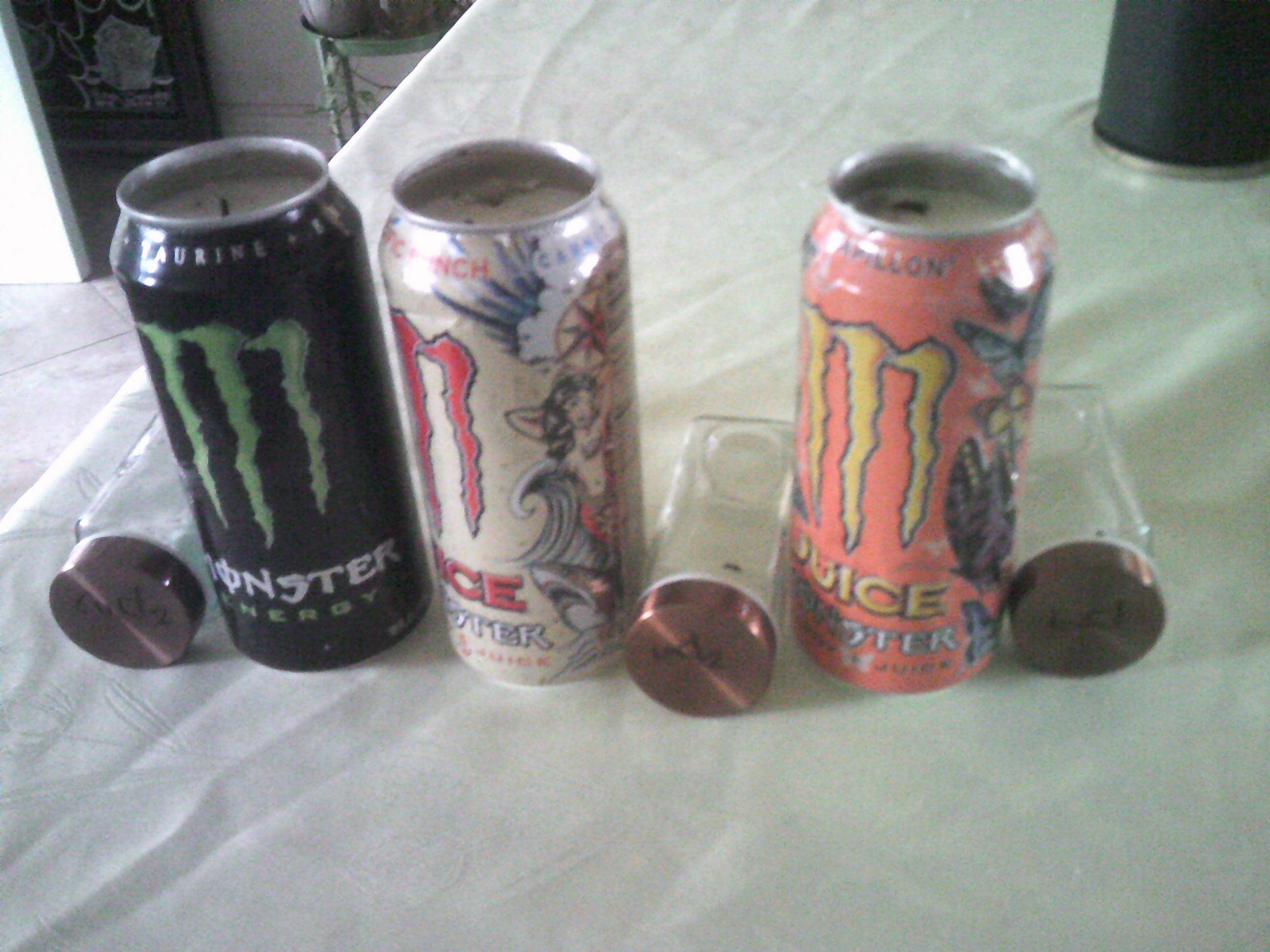 Three cans of monster energy drink turned candles, they are all right next to their respective vials of chemicals that supposedly change the color of fire.