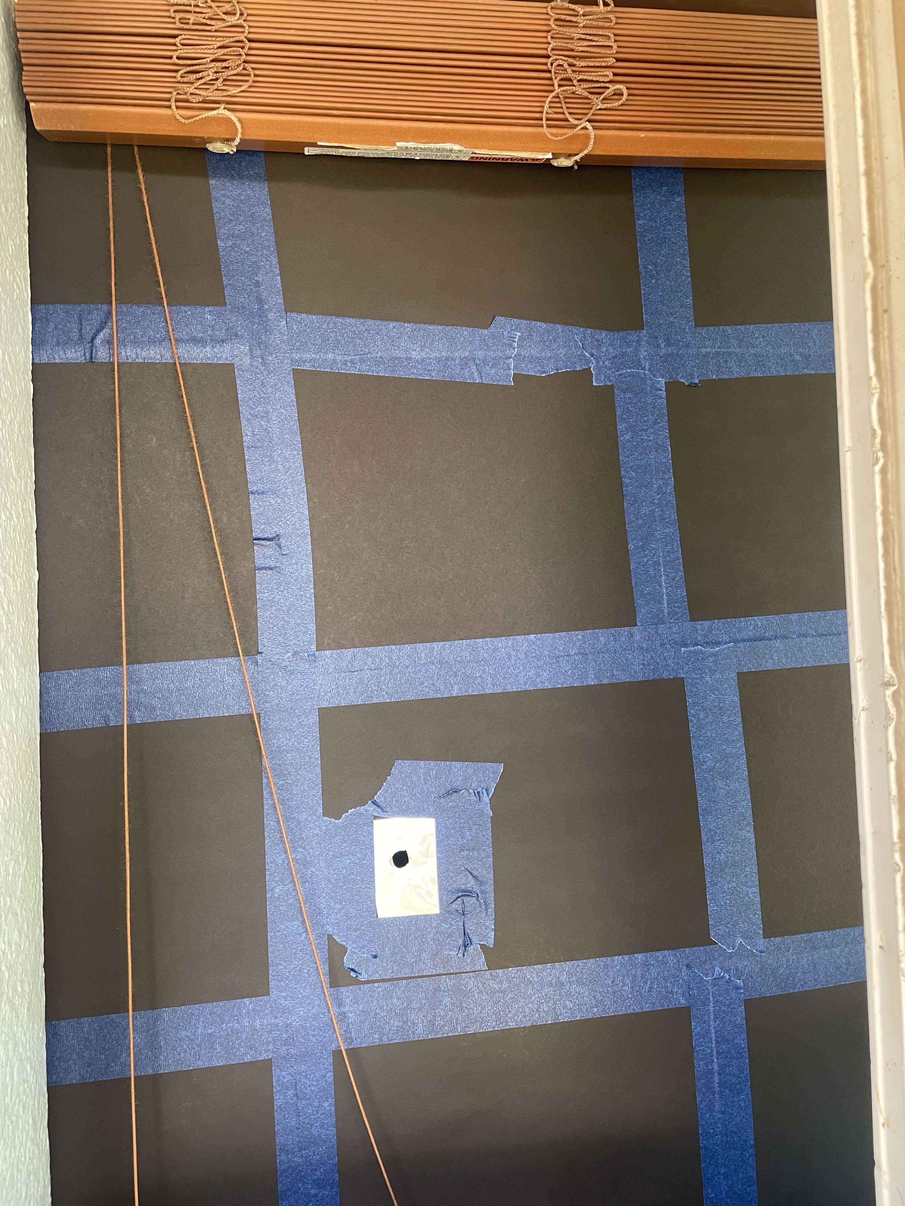 A window blocked out by a huge black paper with a small aluminum apperture at the center.